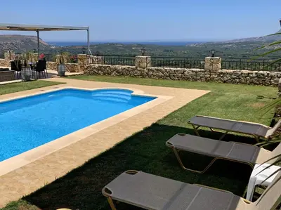 a swimming pool with two lawn chairs next to a house at Villa Vangelis Stylos Crete in Khiliomoudhoú