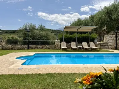 a swimming pool in a yard with chairs and an umbrella at Villa Vangelis Stylos Crete in Khiliomoudhoú