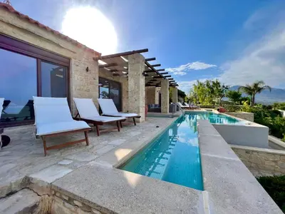 a swimming pool with white chairs next to a house at Villa Elena Chania in Karefilianá