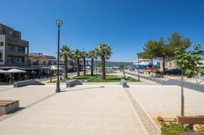 a park with benches and palm trees in a city at Nidus Villa in Souda