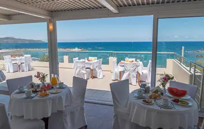 a restaurant with white tables and chairs and the ocean at Porto Alegre Hotel in Kalamaki Chanion