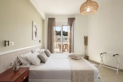 a white bedroom with a large white bed and a window at Artemis Apartments in Stalos