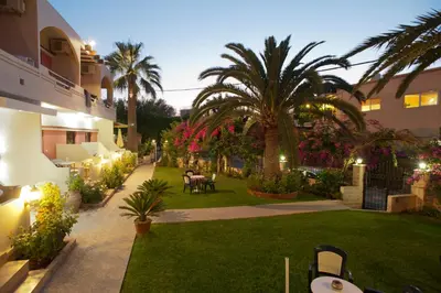 a courtyard of a building with a lawn and palm trees at Nikolas Suites in Kato Daratso