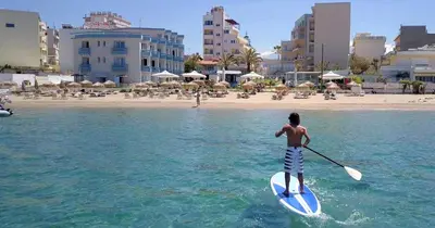 a man on a paddle board in the water near a beach at Hotel Christina in Chania Town