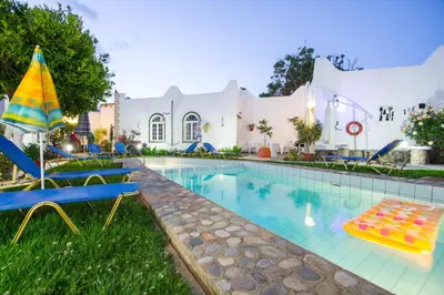 a pool with chairs and an umbrella next to a house at Konaki Apartments in Maleme