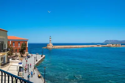 a view of a lighthouse and the water with people walking on the sidewalk at Hotel Amphora in Chania Town