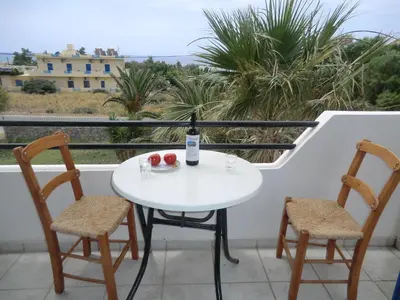 a table with two chairs and a bottle of wine on a balcony at Flisvos Apartments in Frangokastello
