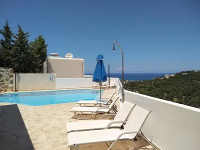 a pool with white chairs and an umbrella on a balcony at Ilios Village in Stalos