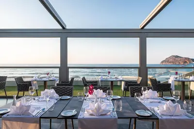 a dining room with tables and chairs and the ocean at Porto Platanias Beach Luxury Selection - Adults Only in Plataniás