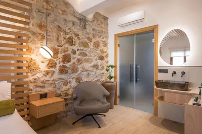 a bedroom with a stone wall with a chair and a mirror at Agave Suites in Chania Town