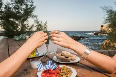 two people sitting at a table with food and the ocean at kito- transformed house on the water's edge in Chania Town