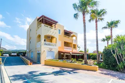 a large yellow building with palm trees in front of it at Thalassa Apartments in Kissamos