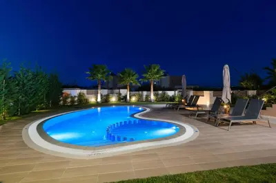 a swimming pool at night with chairs and umbrellas at Villa Thalia in Stalos