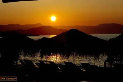 a sunset over a lake with a bunch of chairs at Steps to Nea Chora beach Angela apt ,10min to town in Chania Town