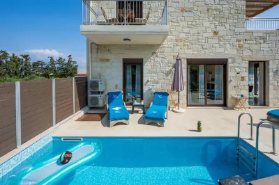 a swimming pool with two blue chairs and a house at Villa Rebecca in Agia Marina Nea Kydonias