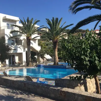 a swimming pool with palm trees in front of a building at Maria Suites in Plataniás
