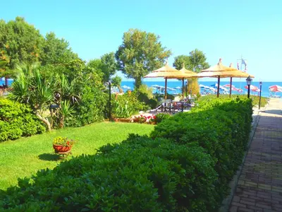 a garden with tables and umbrellas on the beach at Katerina Seaside Studios in Plataniás