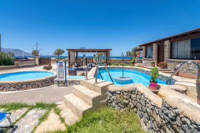a swimming pool in a yard with a stone wall at Drapanias BeachFront Apartments - Marinakis in Kissamos