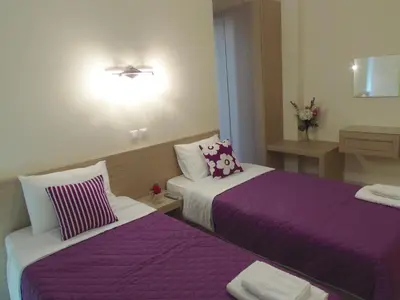 two beds in a hotel room with purple sheets at Angelica Studios and Apartments in Agia Marina Nea Kydonias