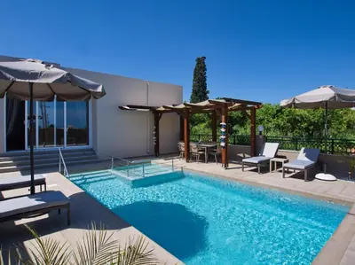 a swimming pool with chairs and umbrellas next to a house at Villa Andreas in Kamisianá