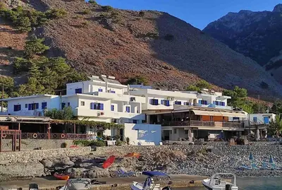 a building on a beach with boats in front of it at Zorbas Studios in Agia Roumeli