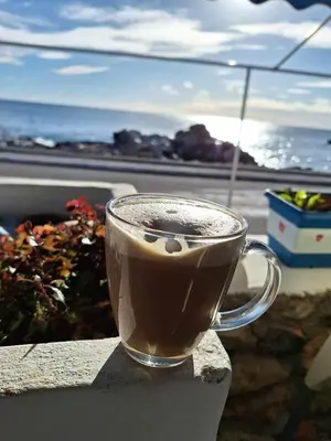 a cup of coffee sitting on a ledge near the ocean at Haris Studios in Palaiochóra