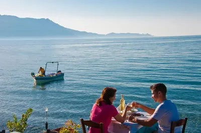two people sitting at a table with a boat in the water at Akrogiali in Kissamos