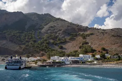 a boat in the water next to a mountain at Giannis Rooms in Agia Roumeli