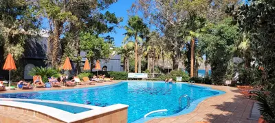 a swimming pool with palm trees and people sitting around it at Marita's Apartments in Agia Marina Nea Kydonias