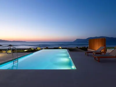 a swimming pool with a view of the ocean at dusk at Youphoria Beach Front Villas in Korfalónas