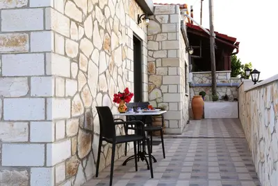 a patio with two chairs and a table against a stone wall at Archontiko Haris in Kolymvari