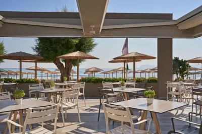 a patio with tables and chairs and umbrellas at Atlantica Amalthia Beach Hotel - Adults Only in Agia Marina Nea Kydonias