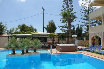 a swimming pool with palm trees and a building at Sunny Suites in Maleme