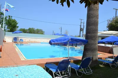 a swimming pool with chairs and blue umbrellas at Sunny Suites in Maleme