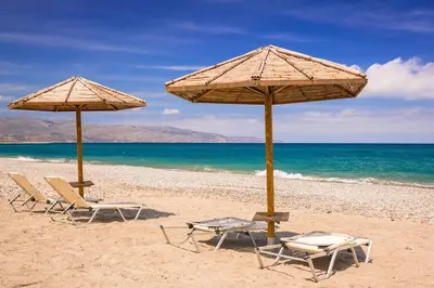 two beach chairs and umbrellas on a beach at Villa Pandora - Petit Bonheur in Maleme