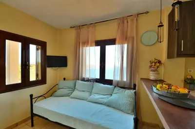 a living room with a blue couch and a window at Kalithea Studio Aptera in Megála Khoráfia
