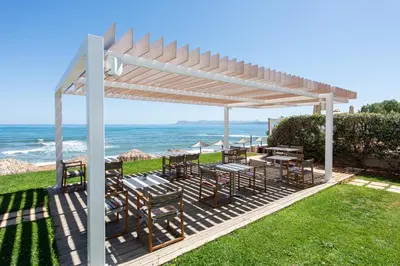 a pergola with tables and chairs and the ocean at The Mini Beach Hotel in Stalos