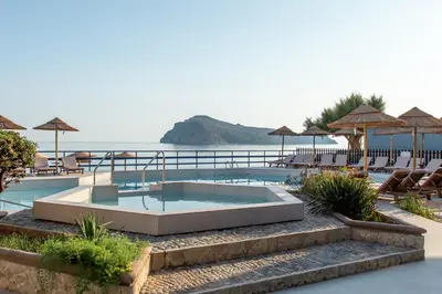 a swimming pool with tables and umbrellas at a resort at Hotel Haris on the beach in Agia Marina Nea Kydonias
