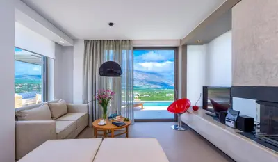 a living room with a couch and a tv and a large window at Youphoria Sea View Villas in Kissamos