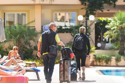 two people walking by a pool with their luggage at Helios Apartments in Kato Daratso