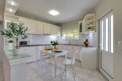 a kitchen with white cabinets and a table and chairs at Chania Elite Homes, Enjoy a Chic Oasis by the heated Pool in Kounoupidhianá