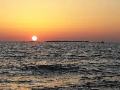a sunset over the ocean with a boat in the distance at Cozy secluded studio with panoramic view in Áyios Yeóryios