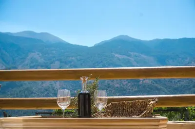 a table with two wine glasses on a balcony with mountains at To Spiti mas in Sougia
