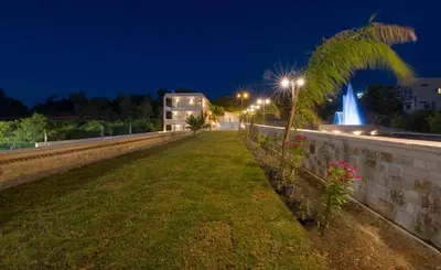 a park at night with a palm tree and a fountain at Queen Electra with pool and tennis court in Alikianós