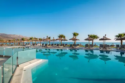 a swimming pool with chairs and umbrellas and the ocean at Solimar White Pearl - Adults Only in Kolymvari