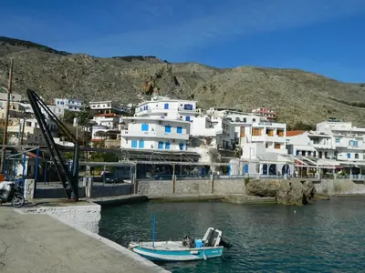 a small boat in the water in front of buildings at Lefka Ori in Khóra Sfakíon