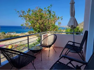 a balcony with chairs and an umbrella and the ocean at 180 Degree Sea View Apartment in Palaiochóra