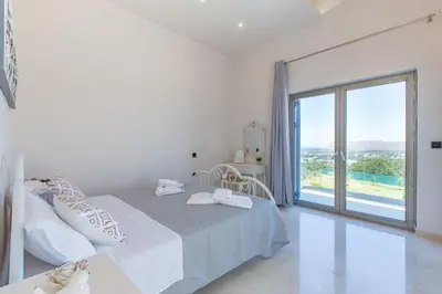 a white bedroom with a bed and a sliding glass door at Villa Kounoupidiana in Kounoupidhianá