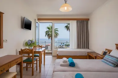 a hotel room with two beds and a dining table and a balcony at Hermes Sea View in Stalos