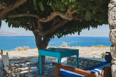 a table under a tree with the ocean in the background at Karavos View - An artists' hideaway Paradise in Kalyves